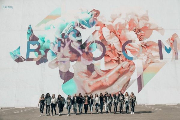 Line of women standing in front of wall mural that says "bloom"