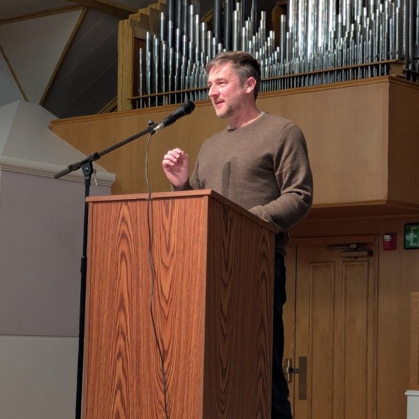 Dan Beachy-Quick stands at a podium, delivering a lecture at Boise State University.