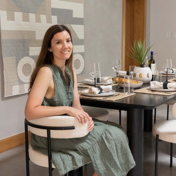 Woman in sage green sleeveless dress sitting at modern black dining table with cream upholstered chairs and geometric wall art in minimalist dining room.