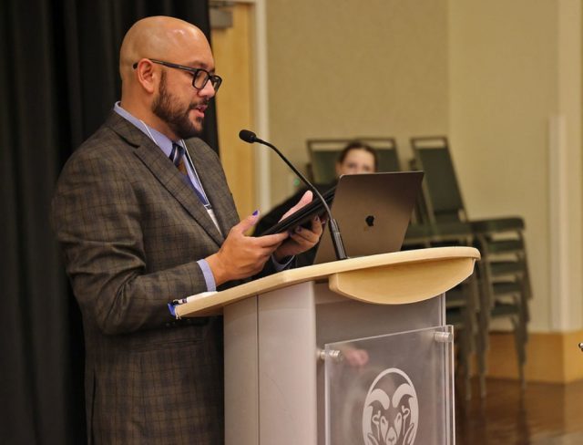 GradShow_web1 Will Brooks presenting at podium with microphone and laptop at Graduate Student Showcase, Nov. 19.