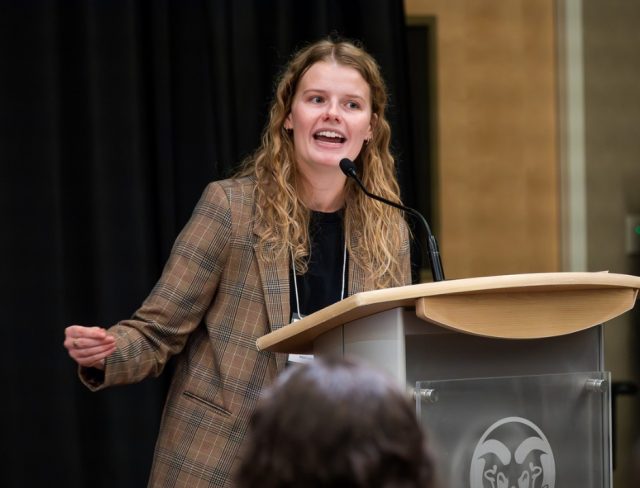 Gradshow_web3 Annie Ness presenting animatedly at podium at Graduate Student Showcase, Nov. 19.