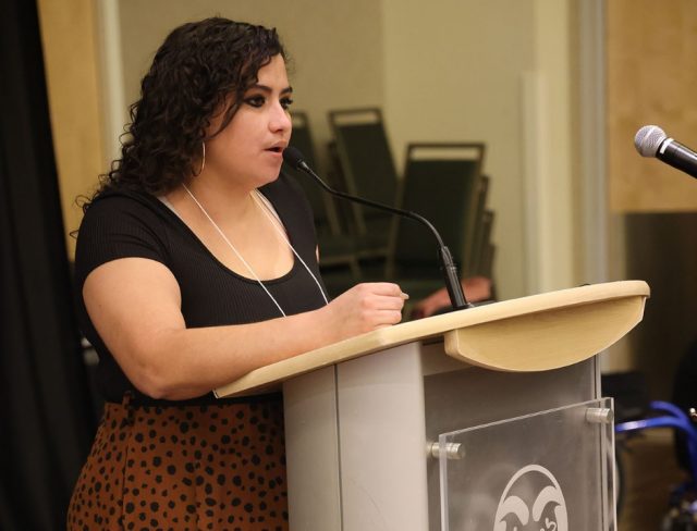 GradShow_web5 Liz Ramirez presenting at podium with microphone at Graduate Student Showcase, Nov. 19.