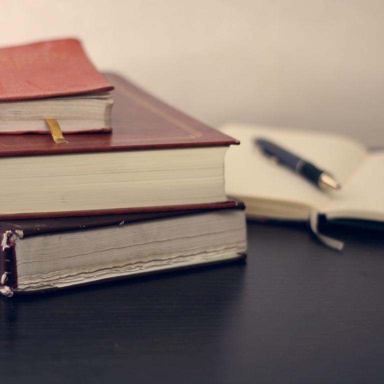Stack of books next to a notebook and pen