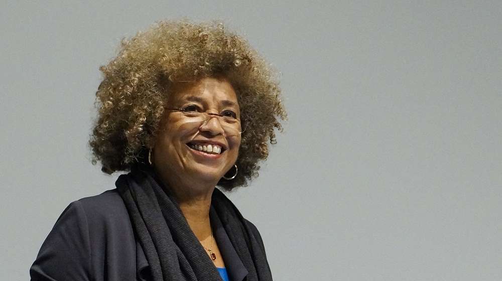 Angela Davis smiling in front of a gray background