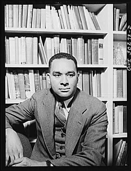 Richard Wright in black and white, wearing a three piece suit and sitting in front of a bookcase