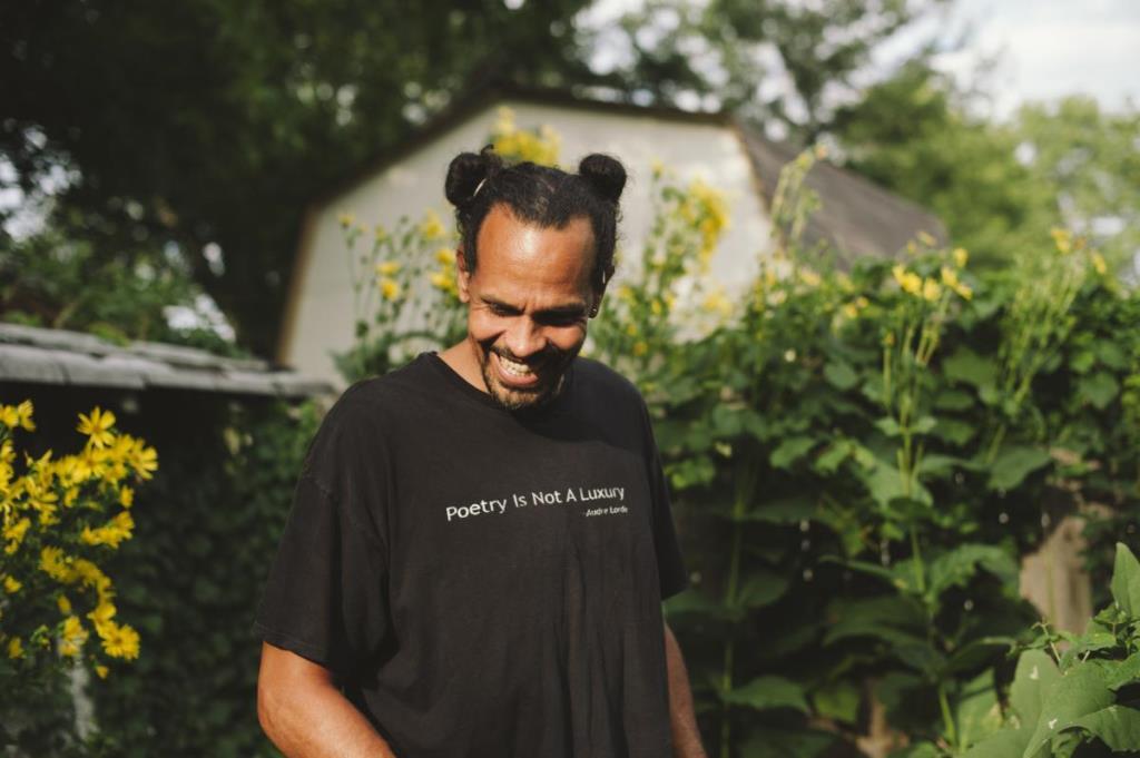 Ross Gay in a garden, looking down and smiling