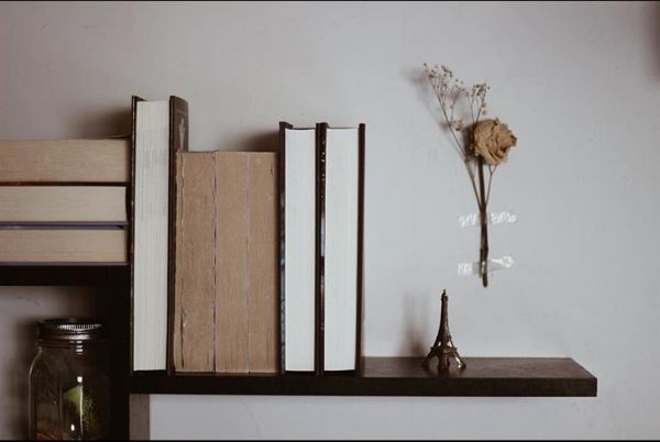 A shelf of books hanging on the wall with dried flowers.