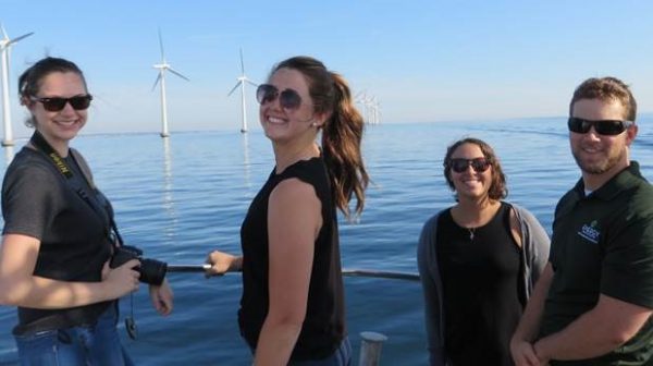 Group of students by the water with wind turbines in the background