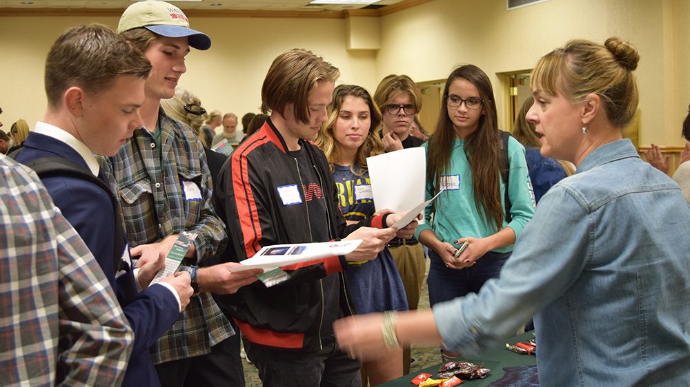 a group of students standing around a presenter, looking at papers at the 2019 possibilities fair