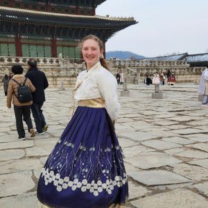 Cairn Carr wears a traditional Korean hanbok (a white top with a navy blue and gold embroidered skirt) while visiting Gyeongbokgung Palace in Seoul, South Korea.