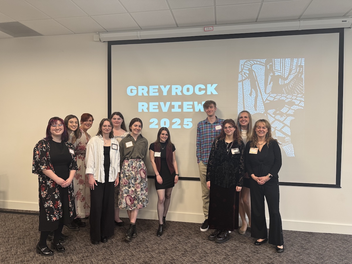 Group of students and staff posing in front of a projection screen displaying "GREYROCK REVIEW 2025" in a conference room setting.