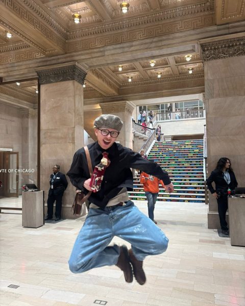 Zach Luiz joyfully jumping in the grand hall of the Art Institute of Chicago, with colorful text-covered stairs visible in the background.