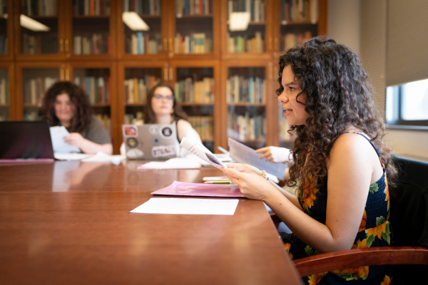 Students gather around a table with papers in front of them during a writing workshop.
