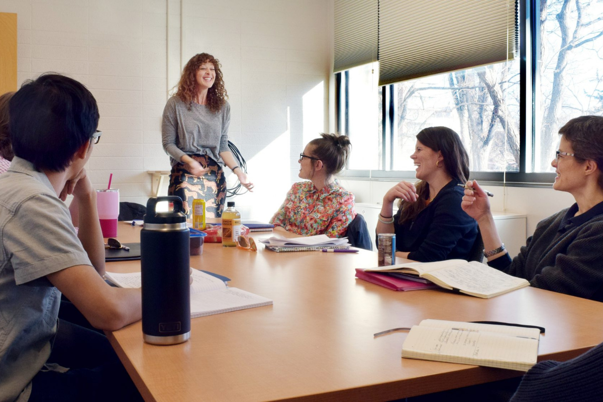 Faculty member and students gather around a table during a writing workshop.