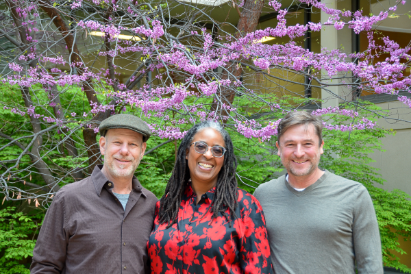 Three faculty members pose outdoors in front of redbud tree in a campus courtyard.
