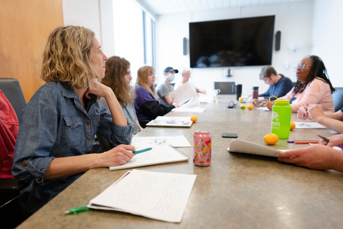 Students and faculty gather around a large table during a writing workshop.